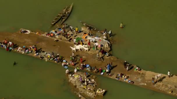 マリを背景に地元の村と川で服を洗っている人々と忙しい農村川沿いの無人偵察機ビュー — ストック動画