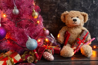 Atmosferik Noel veya yeni yıl kompozisyonu, siyah arka planda pembe Noel ağacı, oyuncak ayı, hediyeler. Boşluğu kopyala