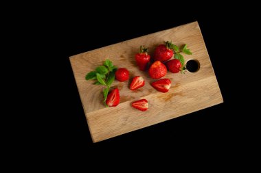 Mutfak tahtasının üzerinde taze nane dalları ve siyah arka planda iştah açıcı parlak çilekler.