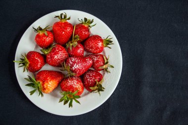 İştah açıcı, parlak çilekler siyah arka planda beyaz bir tabakta - vitamin bileşimi, yazın tadı