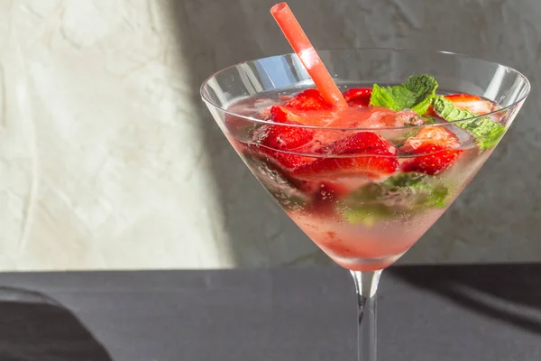 cooling strawberry cocktail with ice and mint on black and concrete background, stylish and tasty, unusual martini
