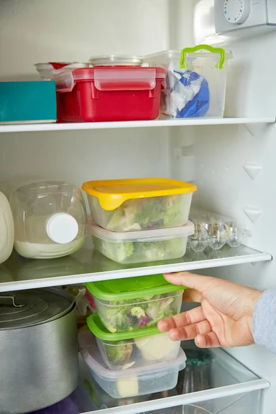 Young man puts trays in the refrigerator. The concept of preparing and storing home or restaurant food for a long time.