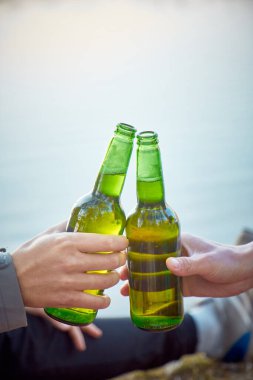 İki şişe bira, erkeklerin elinde köpüklü su. Doğada zaman geçirme kavramı.. 