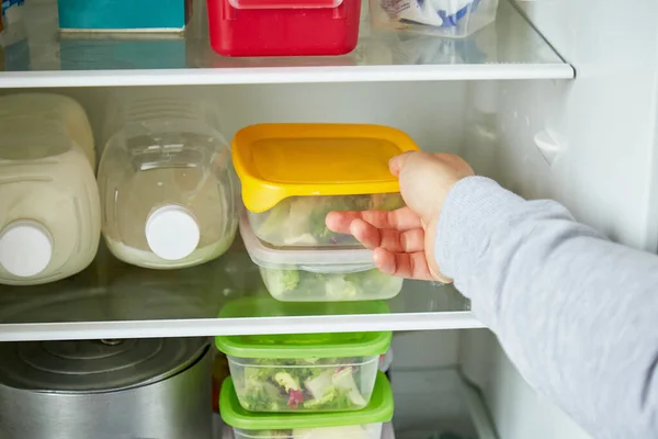 Young man puts containers in the refrigerator. The concept of preparing and storing home or restaurant food for a long time.