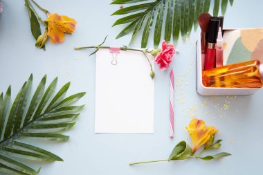 Kırtasiye kartı, kalem, tropik yapraklar, kozmetik ürünleri ve alstromerya çiçekleriyle yaz güzelliği konsepti