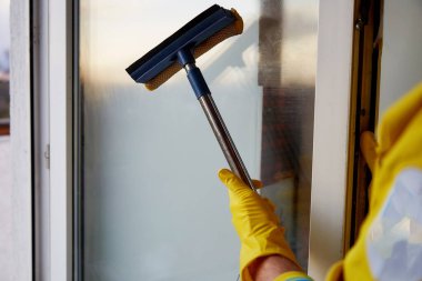 Bahar temizliği konsepti. Salgın yoluyla sterilize et ve temizle, covid 19. Teal ve Turuncu. Akşam ışığında evde cam siliyor.