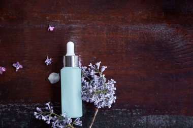 Damlatan cam şişe maketi. Vücut bakımı ve spa. Doğal güzellik ürünleri. Leylak çiçeklerindeki yaşlanma önleyici serum şişesinin şablonu. Doğal sağlık kozmetik ürün konsepti. Boşluğu kopyala