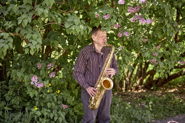 Kiev, Ukraina - 16 maj: En gatusaxofonist spelar trumpet en solig dag i en vårpark. Ledig dag, folkunderhållning — Stockfoto