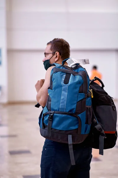 Пассажир в маске с багажом в вестибюле аэропорта. Туризм во время пандемии коронавируса. Размытый фон. — стоковое фото