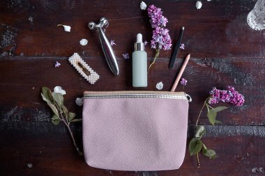 Debriyajlı şık patlama kozmetik aksesuarları: yüz masajı, cımbız, göz kalemi, toka, kadın aksesuarları. Kadınsı yaratıcı konsept. Leylak çiçeği süslemesi. Üst görünüm