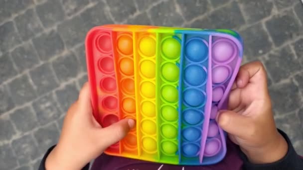 Baby Junge spielt mit Regenbogen sensorischen Fidget. Neues trendiges Silikonspielzeug. Bunte antistress sensorische Spielzeug Fidget schieben es in Kinderhände. Antistress trendiges Pop-it-Spielzeug. — Stockvideo