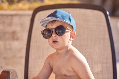 Beyaz, tatlı erkek bebek yüzme havuzunun yanında güneşleniyor. Yaz tatilleri ve eğlence konsepti