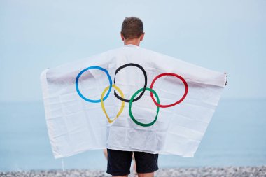 Kemer, Türkiye - 16 Haziran 2021: İnsan deniz kıyısında Olimpiyat bayrağıyla kaplıdır. Olimpiyat oyunları konsepti. Umut ve başarı kavramı. Yüksek kalite fotoğraf