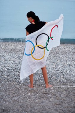 Kemer, Türkiye - 16 Haziran 2021: Kadın deniz kıyısında Olimpiyat bayrağıyla kaplandı. Olimpiyat oyunları konsepti. Umut ve başarı kavramı. Yüksek kalite fotoğraf