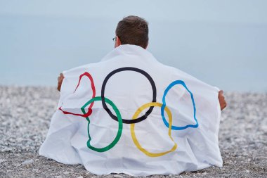 Kemer, Türkiye - 16 Haziran 2021: İnsan deniz kıyısında Olimpiyat bayrağıyla kaplıdır. Olimpiyat oyunları konsepti. Başarı umudu ve inanç kavramı