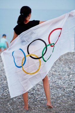 Kemer, Türkiye - 16 Haziran 2021: Kadın deniz kıyısında Olimpiyat bayrağıyla kaplandı. Olimpiyat oyunları konsepti. Başarı umudu ve inanç kavramı