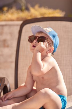 Beyaz, tatlı erkek bebek yüzme havuzunun yanında güneşleniyor. Yaz tatilleri ve eğlence konsepti