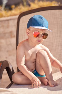 Beyaz, komik, sevimli erkek bebek yüzme havuzunun yanında güneşleniyor. Yaz tatilleri ve eğlence konsepti