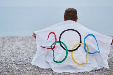 Kemer, Türkiye - 16 Haziran 2021: İnsan deniz kıyısında Olimpiyat bayrağıyla kaplıdır. Olimpiyat oyunları konsepti. Başarı umudu ve inanç kavramı