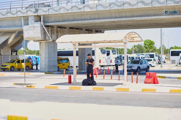 Antalya, Türkiye - 26 Mayıs 2021: Parlak güneşli bir günde havaalanı bölgesinde bir otobüs durağında gözlüklü ve kulaklıklı genç adam