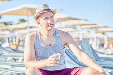 Genç beyaz bir adam yaz havasında plastik bir bardak birayla dinleniyor. Yaz tatili kavramı.