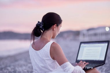 Kumsalda güneşli bir yatakta dizüstü bilgisayarı olan genç bir esmer. Serbest çalışan, uzaktan çalışan, giyimli, konsept öğrenen, arkadaşlarıyla sohbet eden. Yeni normal kavram.