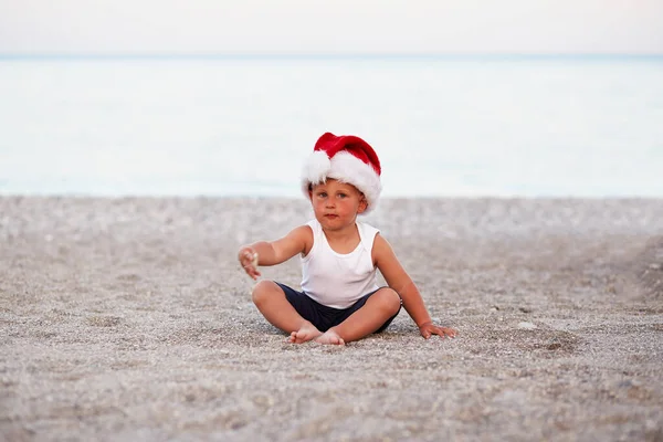 Little caucasian boy is celebrating New Years Eve or Christmas on the beach, seaside. Holiday concept, Christmas mood — 스톡 사진
