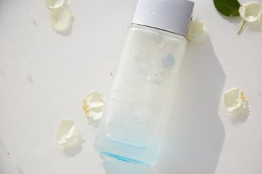 Parfüm bardağı şeffaf şişe, beyaz gül yaprakları ve yaprakları ile suda taklit edilir. Yüksek açılı gölgeler. Üst Manzara. Mesaj için yer. Yüksek kalite fotoğraf