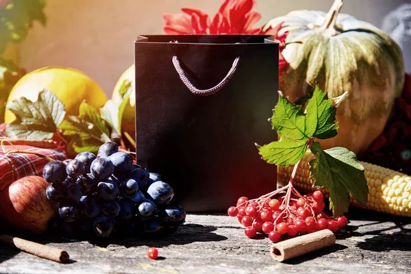 Autumn creative mock up of gift bag among fruits and vegetables, pumpkin, corn, pears, grapes, viburnum and melon. Thanksgiving Day concept. Autumn aesthetic still life with trendy natural shadows.