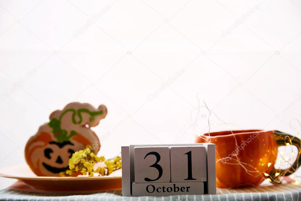 Happy Halloween still life with pumpkin cup and homemade cookies in shape of cute pumpkins and date of Halloween Day. Atmospheric aesthetic autumn holiday concept. Rural life