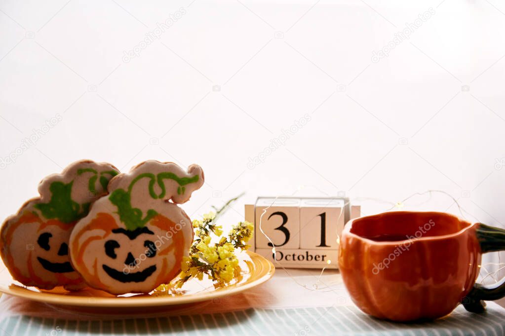 Happy Halloween still life with pumpkin cup and homemade cookies in shape of cute pumpkins and date of Halloween Day. Atmospheric aesthetic autumn holiday concept. Rural life