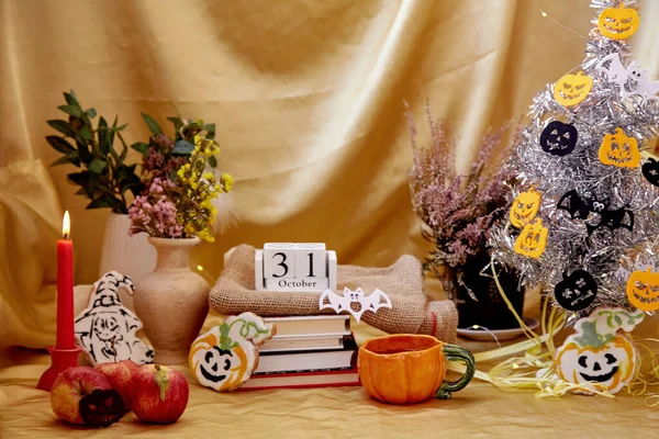 Festive party atmosphere with modern Halloween tree. Cozy Halloween decorations with candles, orange mug, dry flowers, homemade cookies in shape of pumpkin and ghost with books and calendar. — Stock Photo, Image