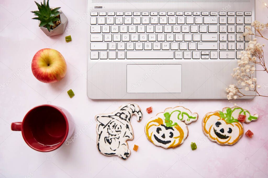 Home office concept on Halloween : laptop and red cup, apple, homemade cookies in shape of cute pumpkins and ghost. Atmospheric working autumn mood 