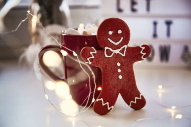 Ev yapımı zencefilli kurabiye, üzerinde şenlikli bokeh dekoru var. Kar arka planda kalsın. Sıcak içecek ve marşmelovlu Noel süsleri. Estetik Noel atmosferi, ev konforu, sıcaklık konsepti