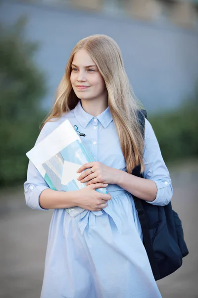 長いブロンドの髪をした美しい十代の女の子の学生の肖像画 学校の初日だ 外の写真 バックパック ノートブック 教科書付きの青いドレスのモデル — ストック写真