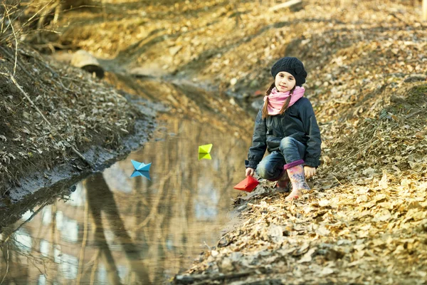 Dívka na břehu řeky hraje papírových lodiček — Stock fotografie