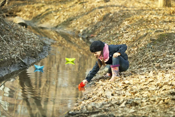 Девушка на берегу реки играет в бумажную лодку — стоковое фото