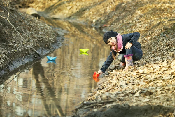 Dívka na břehu řeky hraje papírových lodiček — Stock fotografie