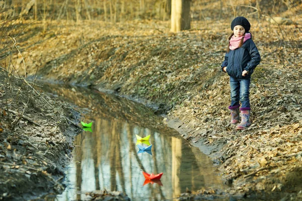 Dívka na břehu řeky hraje papírových lodiček — Stock fotografie