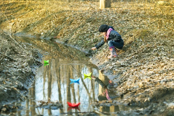 Dívka na břehu řeky hraje papírových lodiček — Stock fotografie