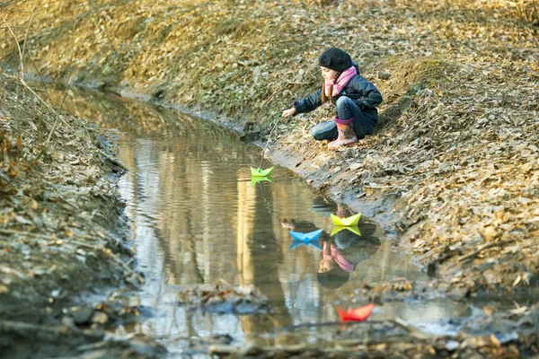 Девушка на берегу реки играет в бумажную лодку — стоковое фото