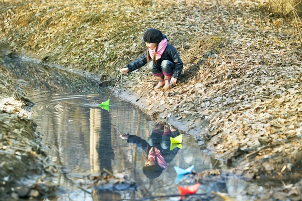 Dívka na břehu řeky hraje papírových lodiček — Stock fotografie