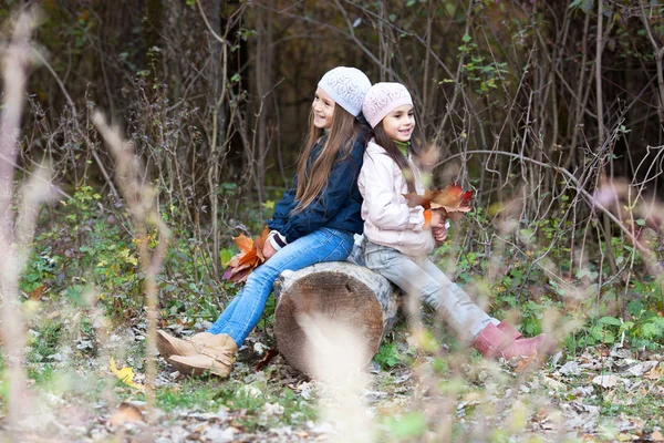 Zwei schöne Mädchen mit Baskenmütze sitzen auf Baumstamm posieren — Stockfoto