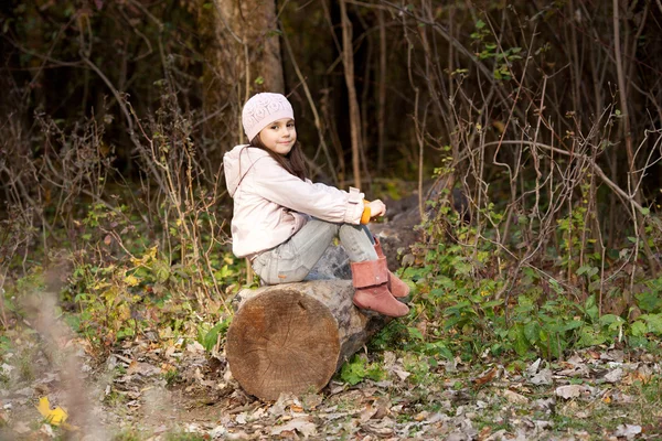 Fille assise sur une bûche dans les bois — Photo