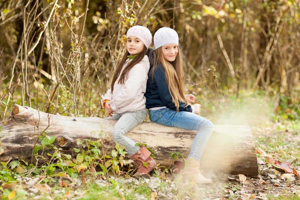 Zwei schöne Mädchen mit Baskenmütze sitzen auf Baumstamm posieren — Stockfoto