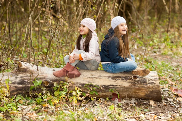 Zwei schöne Mädchen mit Baskenmütze sitzen auf Baumstamm posieren — Stockfoto