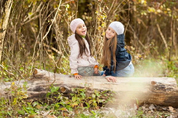 Zwei schöne Mädchen mit Baskenmütze sitzen auf Baumstamm posieren — Stockfoto