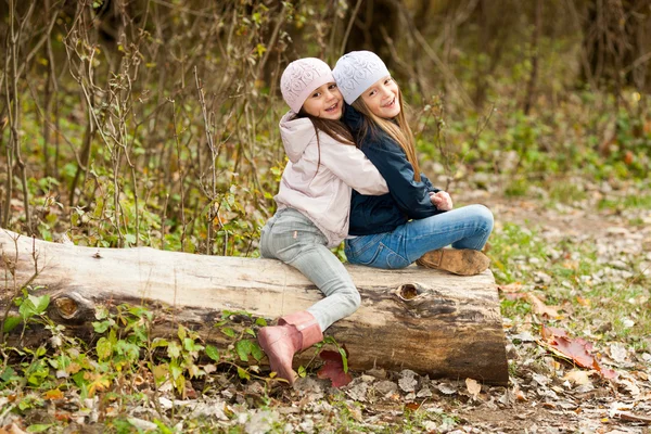 Dua gadis cantik mengenakan baret duduk di kayu berpose — Stok Foto