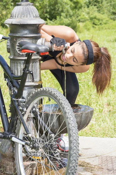 Athletische Frau mit Fahrrad trinkt nach dem Sport Wasser, im Freien. — Stockfoto