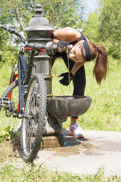 Athletische Frau mit Fahrrad trinkt nach dem Sport Wasser, im Freien. — Stockfoto